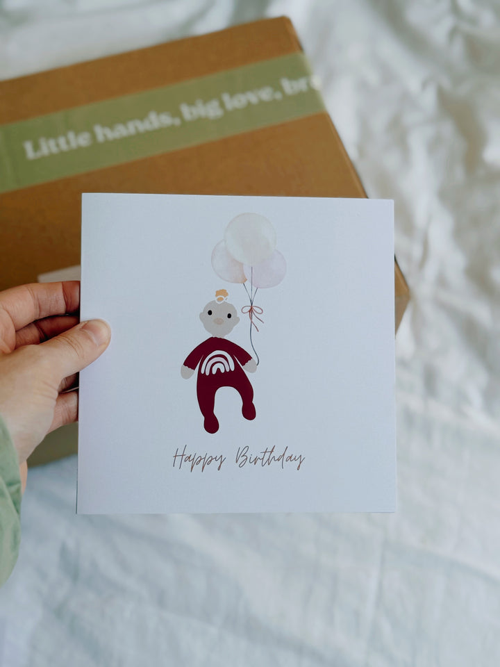Hand holding a little girls birthday card with a bear illustration and 'Happy Birthday' text, with a blurred background. could be for first birthdays. 