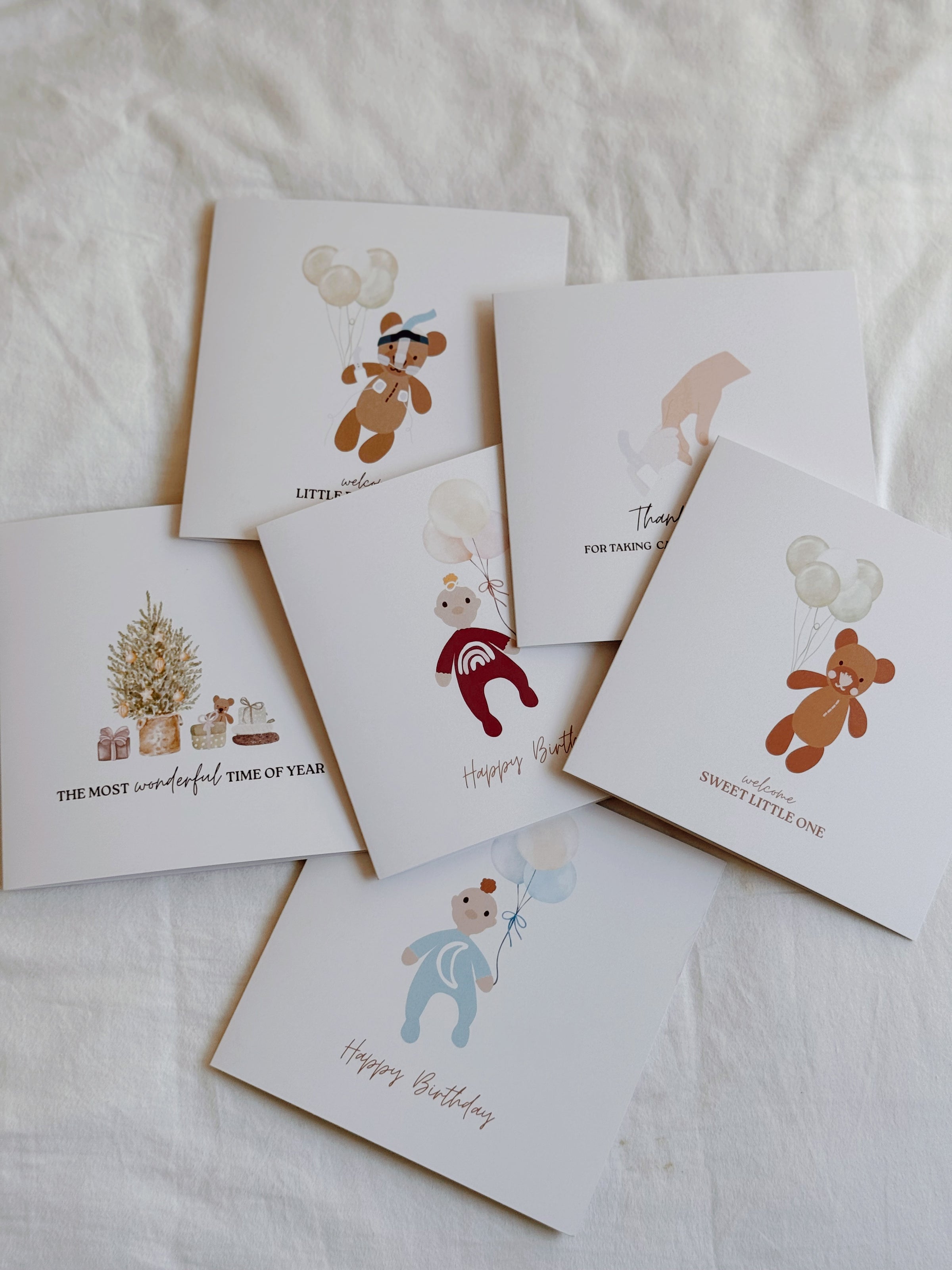Collection of greeting cards with illustrations on a light background. Hand holding a little girls birthday card with a bear illustration and 'Happy Birthday' text, with a blurred background. could be for first birthdays. 